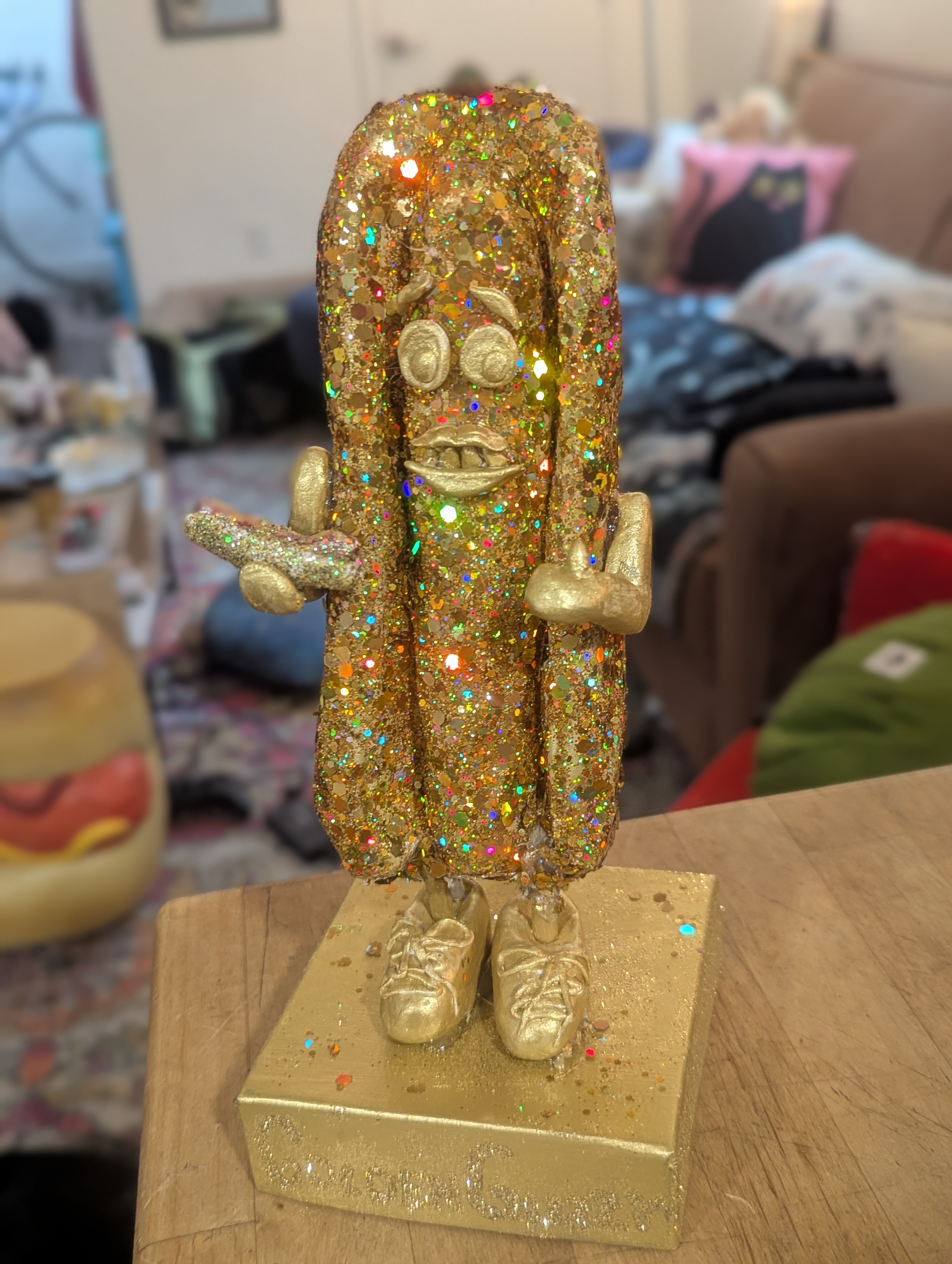 A trophy of a anthropomorphic hotdog, smiling, giving a thumbs up, and holding a smaller hotdog. Very glittery.